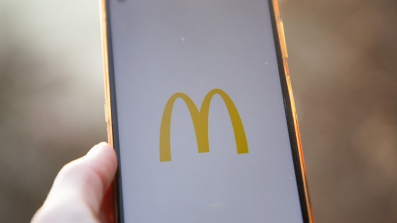 A person's hand is shown holding an iPhone that is loading the McDonald's rewards app.