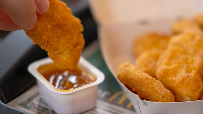 A customer dipping a McDonald's chicken nugget into sauce on a tray at McDonald's.