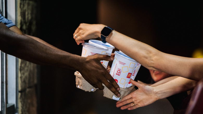a McDonald's drive-thru employee hands drinks to a customer