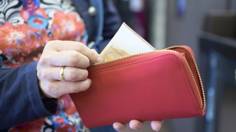 woman's hand with wedding band pulling money from a red purse