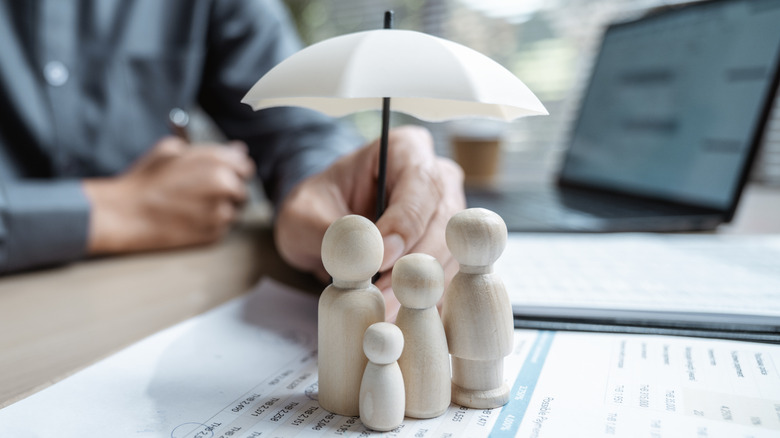 Insurance illustration using wooden figurines huddled under a white umbrella