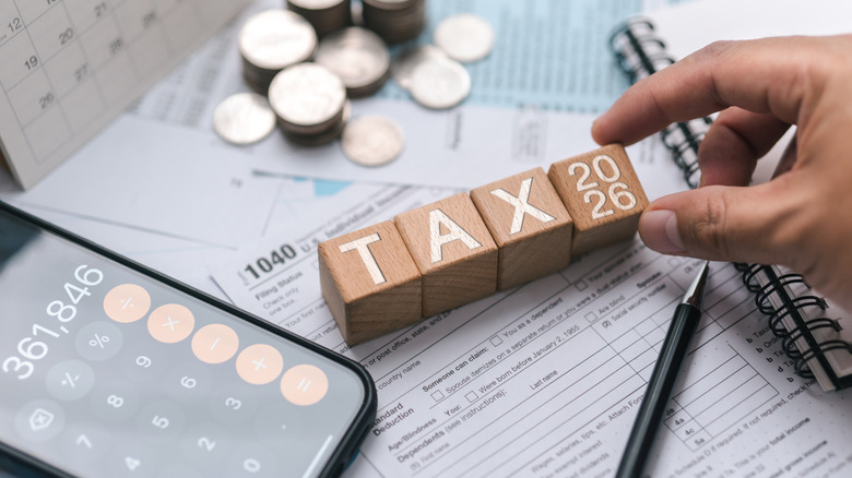Wooden blocks spell out "TAX" next to a phone calculator