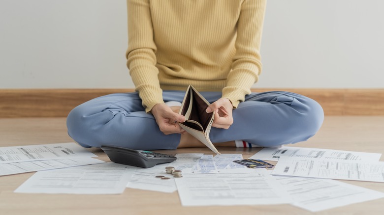 Person with empty wallet surrounded by bills