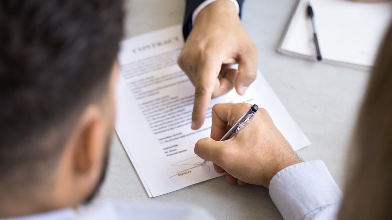young man signing a contract while a realtor points to the signature line