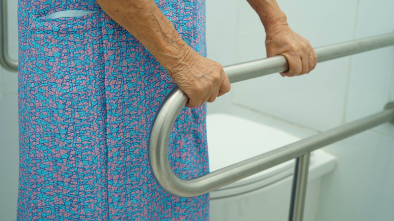 Older woman standing in bathroom grips grab bars next to toilet
