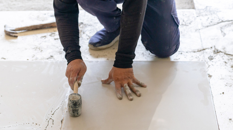 Construction worker uses rubber mallet on tile floors