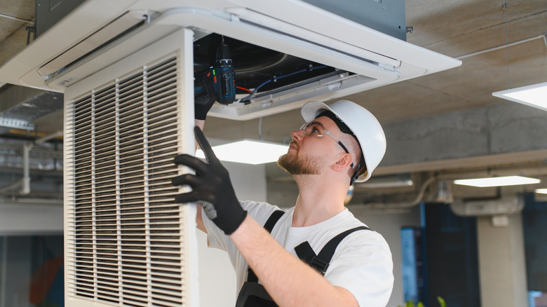 HVAC technician opens ceiling vent to make system repairs