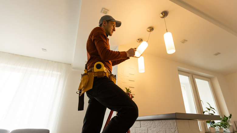 Electrician on ladder renovates home's interior lighting