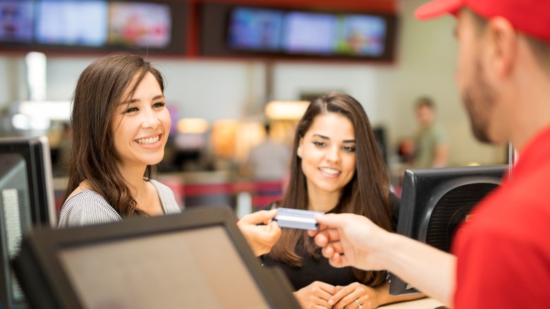Two women hand a credit card to an employee at a movie theater counter
