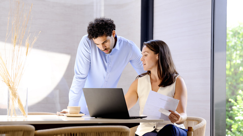A couple scrutinizing financial documents in front of a laptop in their dining room.