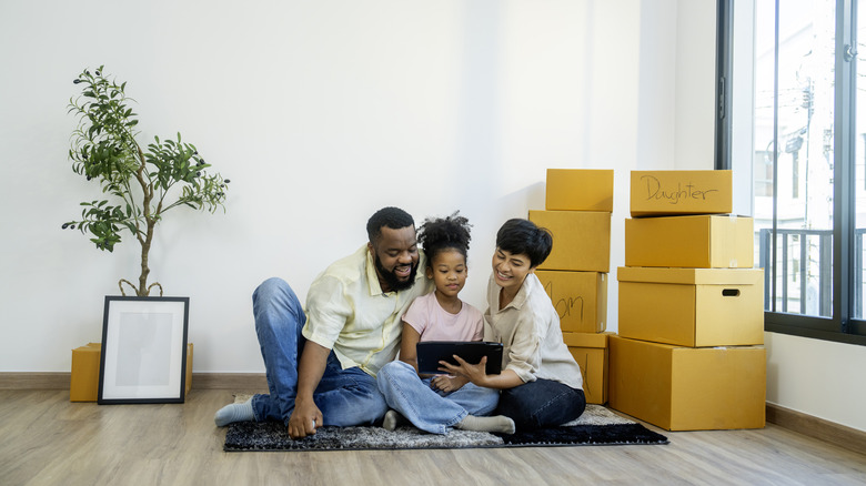 A family seated on the finished floor of their new home next to marked cardboard boxes.