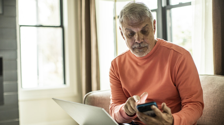 Senior man using laptop computer and smartphone at home