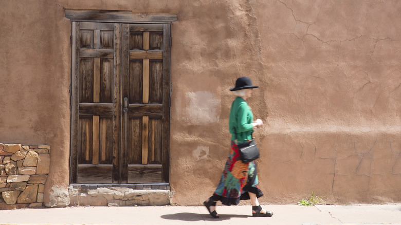 Older woman walking by southwestern looking building.