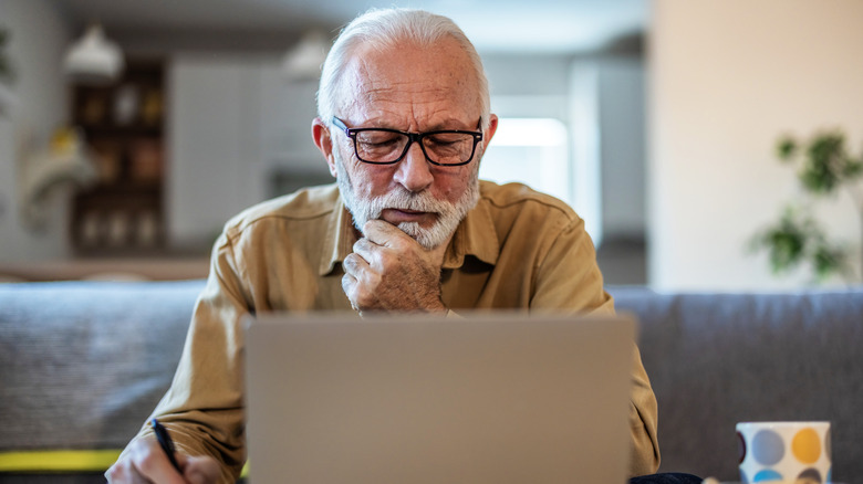 A retired man doing paperwork on his laptop