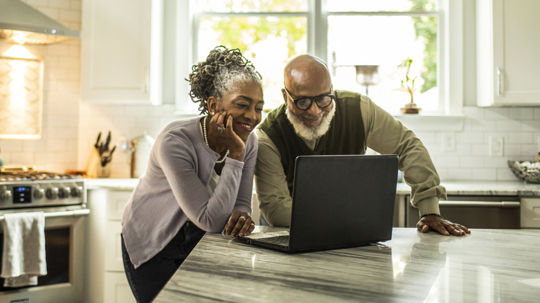 Senior couple using laptop in kitchen of suburban home