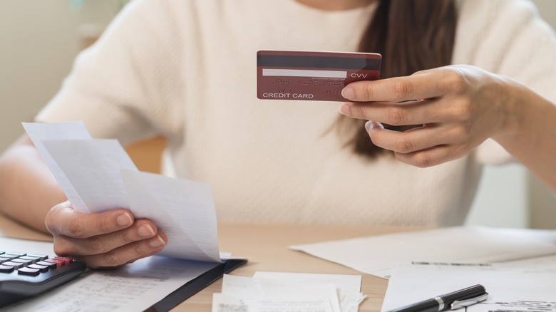 A woman in a white t-shirt looking at credit card statements and bills.