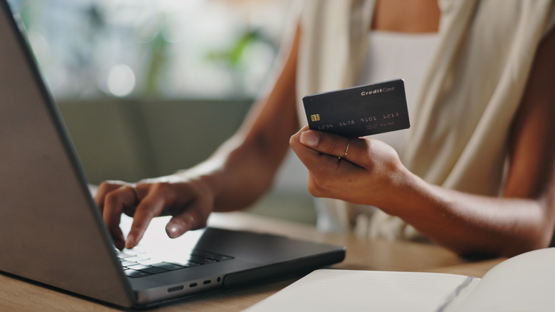 Woman looking at credit card while using her laptop.