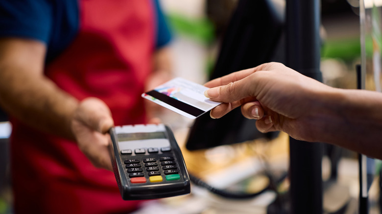 Person holding credit card to tap-to-pay on a credit card machine.