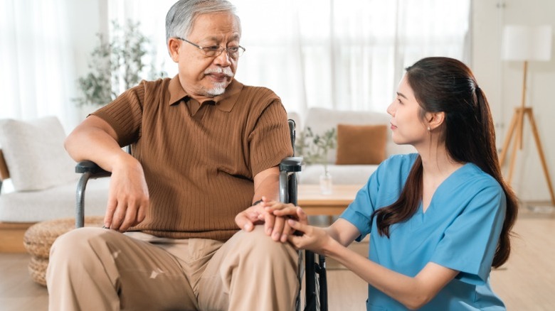 A female home health aide assisting an older male patient at home.