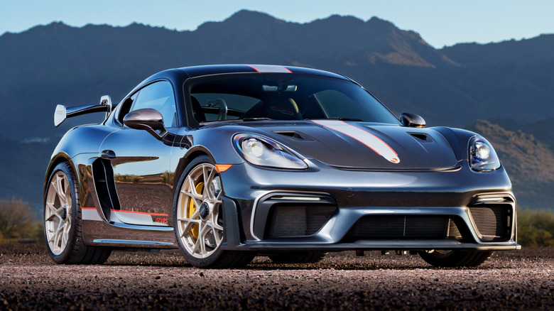A black Porsche Cayman with a white racing stripe parked in the desert