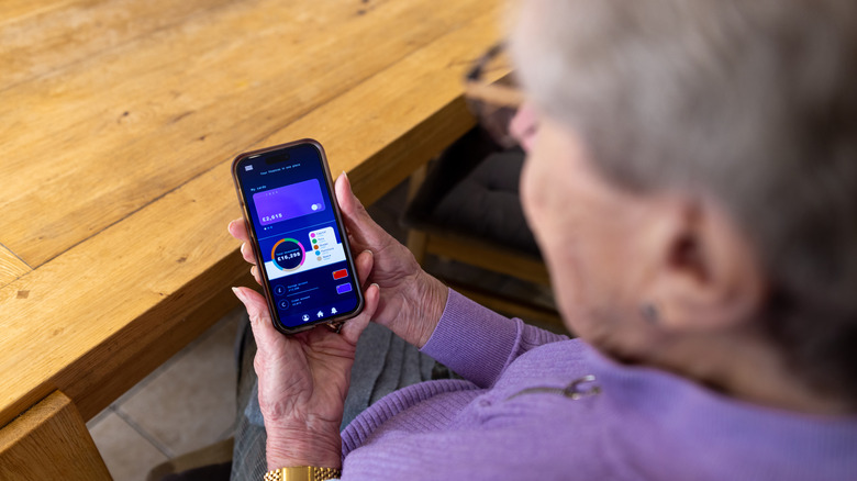 A senior woman holding a smartphone with the screen open to a financial app.