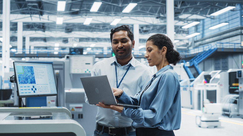 A pair of make and female coworkers looking at a laptop in an industrial manufacturing plant.