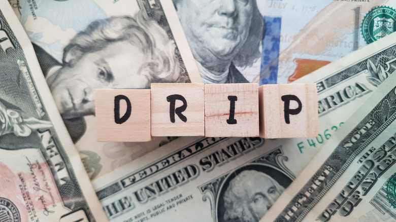 Four wooden blocks with letters D, R, I, and P over bills