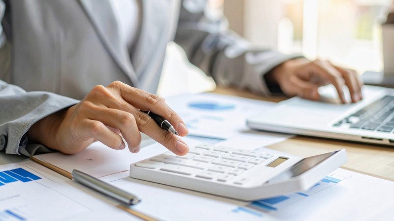 Close up torso a man in casual business suit seated while using calculator and typing on laptop