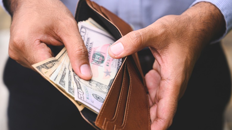 A man wearing a button-down shirt and slacks pulling cash out of a full wallet.