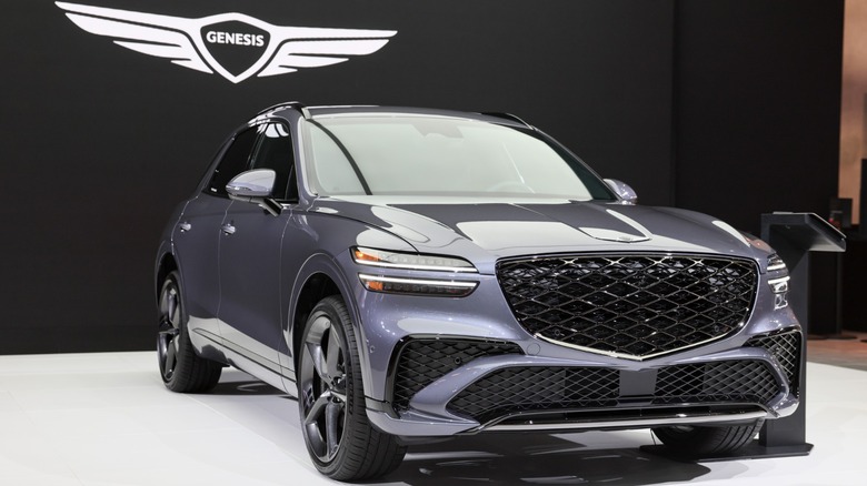 Gray Genesis GV70 luxury SUV displayed beneath the Genesis logo at an auto show