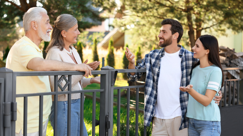 Friendly relationship with neighbours. Young family talking to elderly couple near fence outdoors