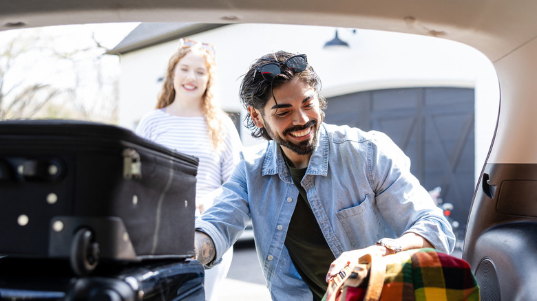 A couple smiling as they put luggage in the back of a hatchback