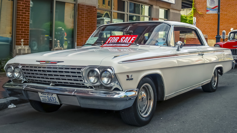 A vintage car with a "For Sale" sign on the windshield