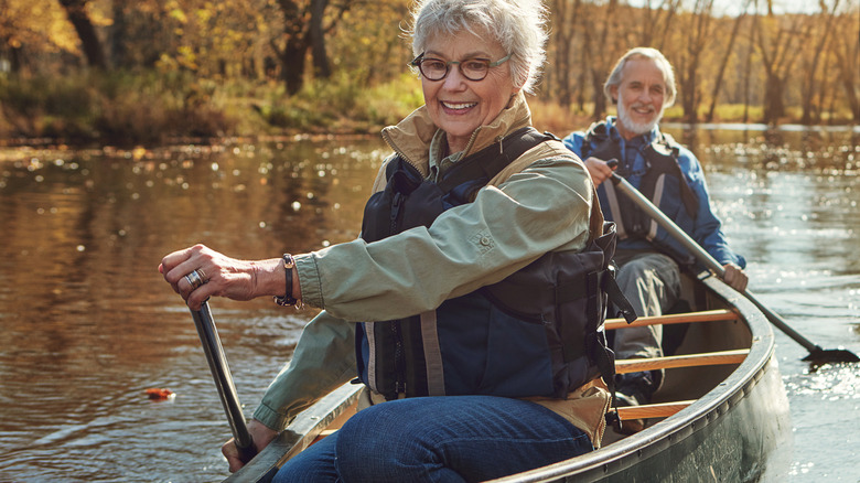 A senior woman and man kayaking on a reflective lake.