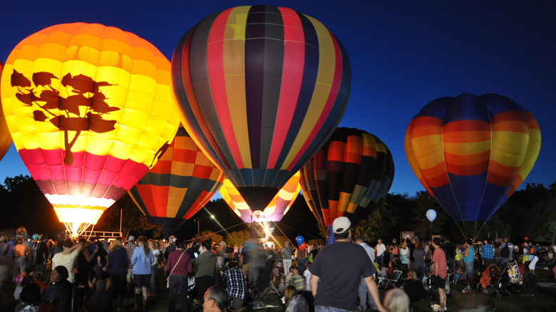 Multiple hot air balloons and people
