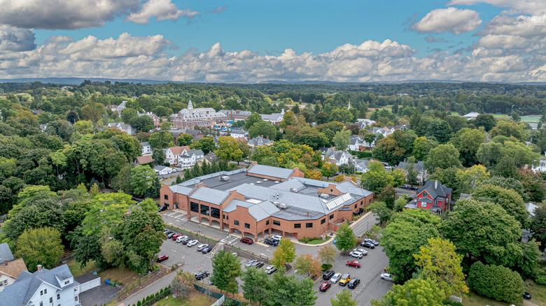 A closer aerial view of Wallingford. Filled with trees, a blue sky, and a large structure with cars parked around it.