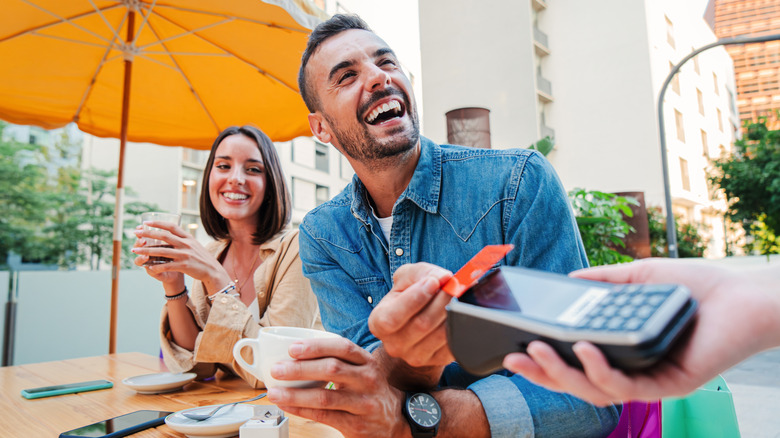 A happy couple paying for drinks with a credit card at a restaurant.
