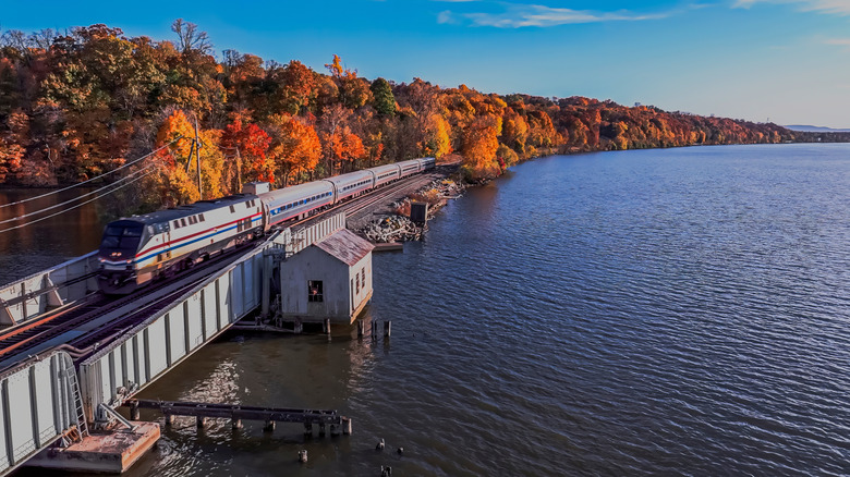 A stunning view of the Hudson River valley, water rippling and trees in autumnal flair, as an Amtrak train cuts through the scene.