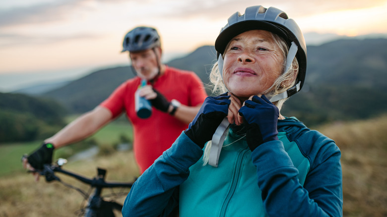 Happy older man & woman ride bikes; mountains in background