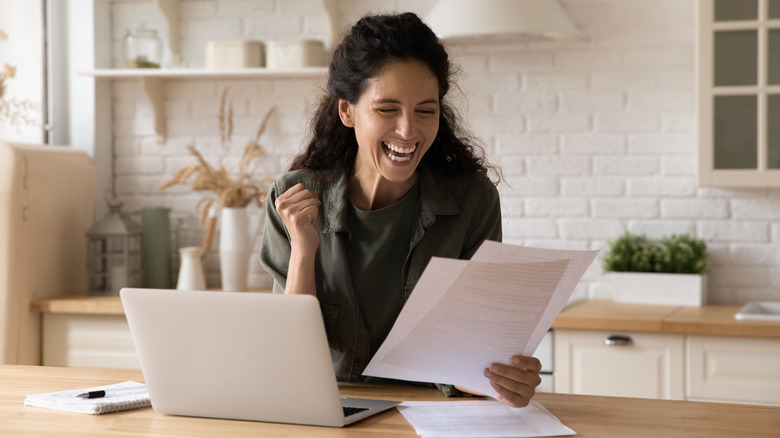 An overjoyed woman reading documents in front of an open laptop.