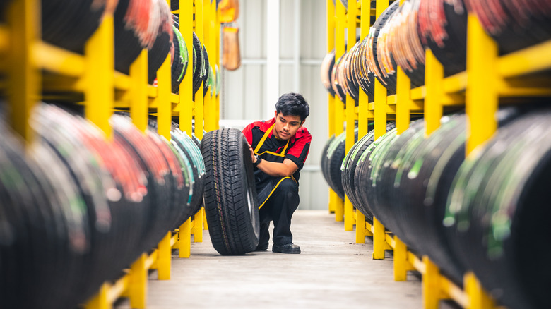 mechanic leaning a tire against a warehouse shelf lined with more tires