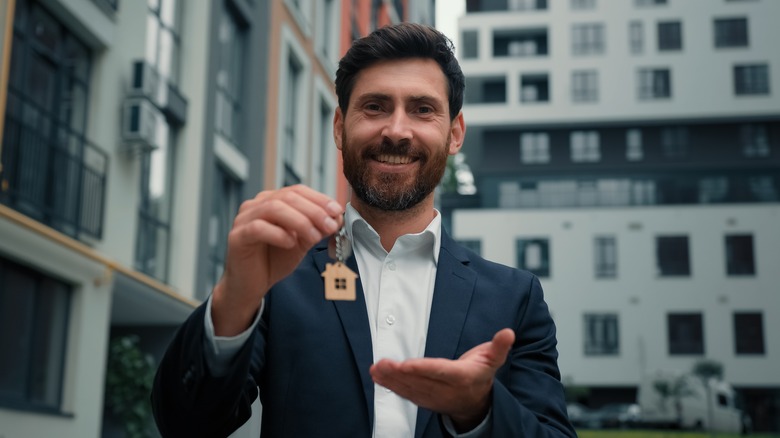 a smiling holds a keychain in the shape of a house