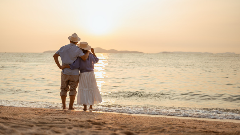 A retired couple watching the sunset from a beach.