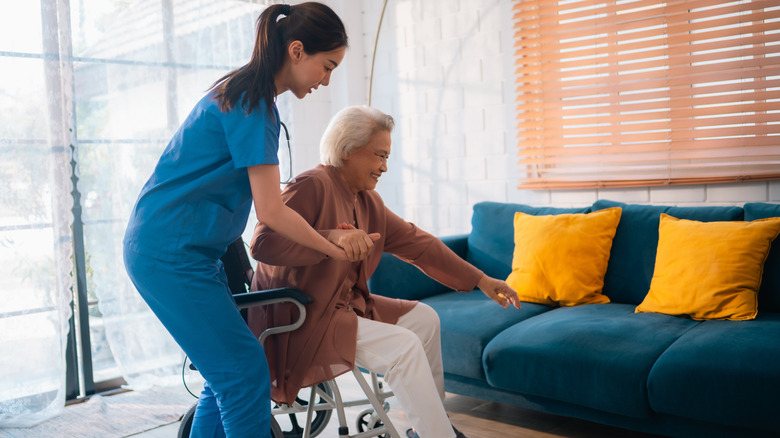 A nurse helping an elderly patient get out of her wheelchair at home.