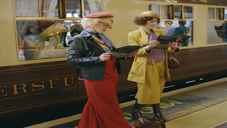 Two persons reading magazines while standing in from of the Pullman train