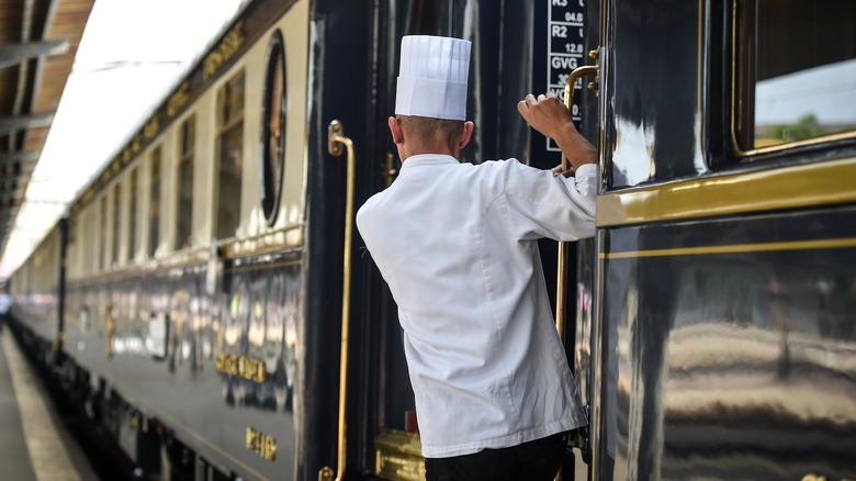 A chef hanging outsid the door of a luxury train.