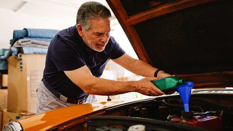 A frustrated retirement-age man putting oil in a car