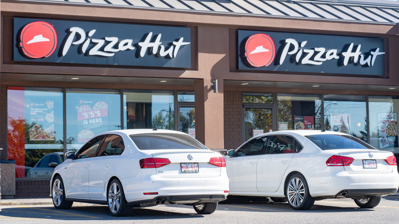 Two white sedans parked outside of a Pizza Hut location with two signs
