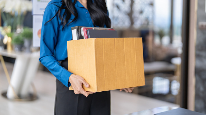 A young woman carriers a box of her possessions as she leaves her office