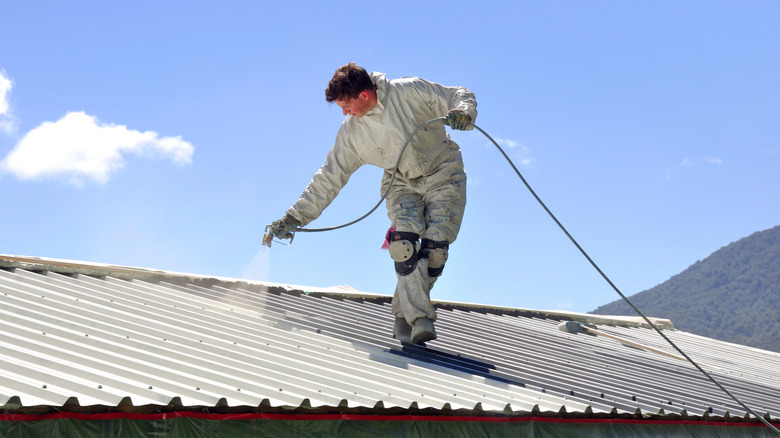 Man spray painting a metal roof white
